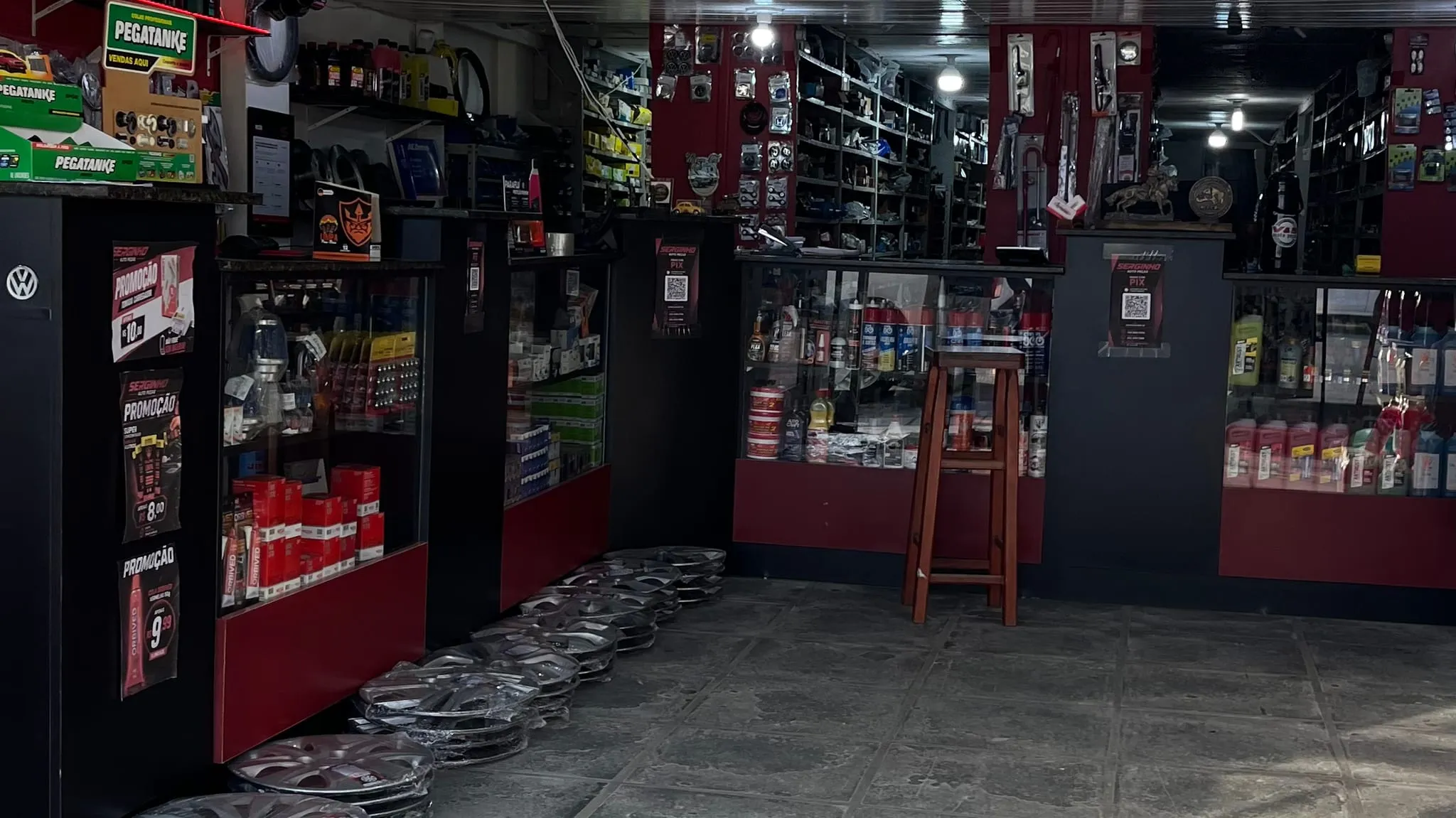 Balcão da Serginho Autopeças, com vitrines de acessórios, calotas empilhadas no chão e prateleiras de peças ao fundo