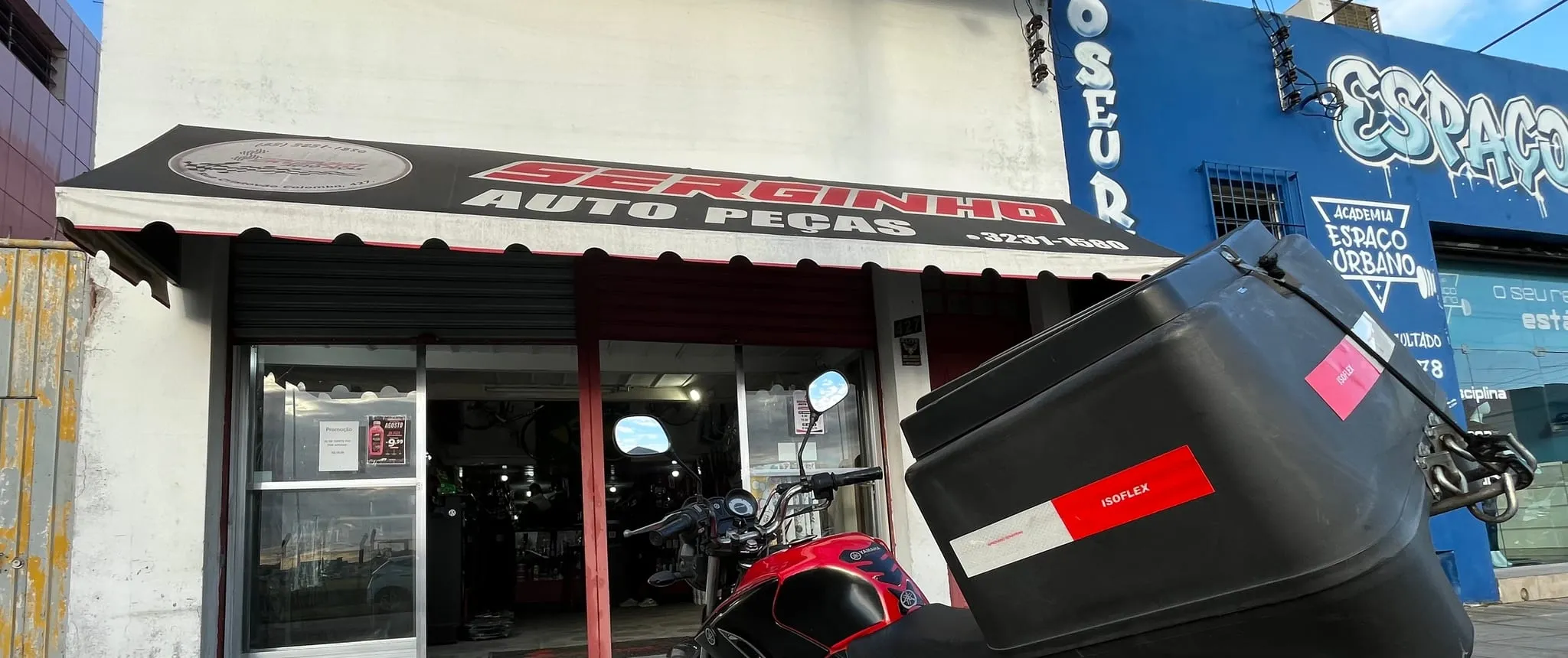 Moto de entrega da Serginho Autopeças, com baú, estacionada na porta da loja